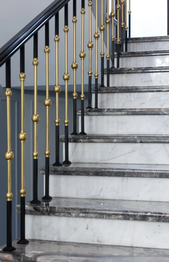 Detalle de una elegante barandilla de hierro forjado con acabados dorados sobre escalera de mármol. Trabajo realizado por expertos en estructuras metálicas y cerrajería en Madrid, combinando seguridad y estética.